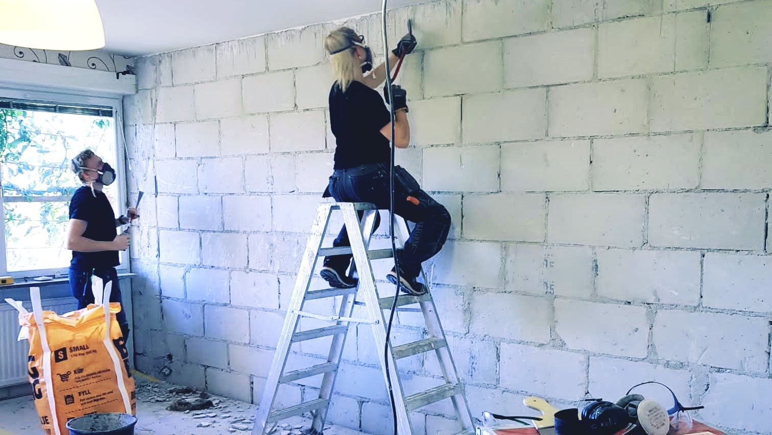 två arbetare som renoverar murad vägg